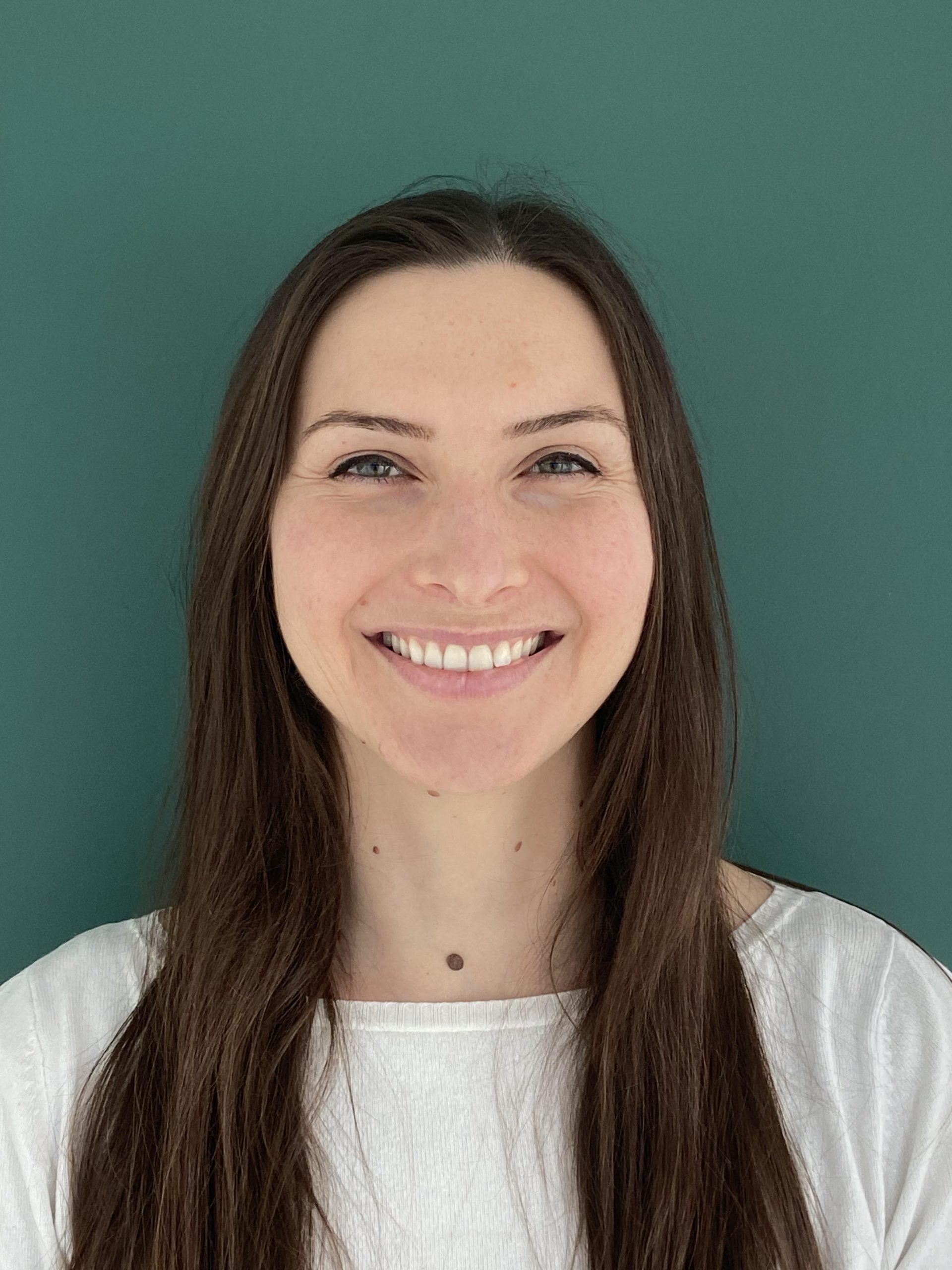 Docteur Lise Daviet, orthodontiste, aux longs cheveux bruns sur fond vert, portant une chemise blanche.