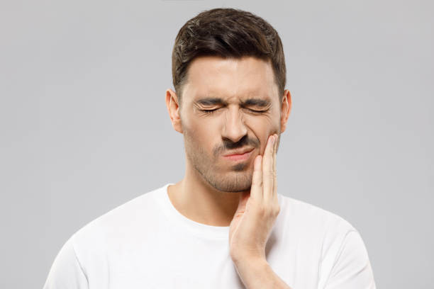 illustration arc blessant Un homme en chemise blanche grimace et touche sa joue avec une douleur apparente à la dent, sur fond gris.