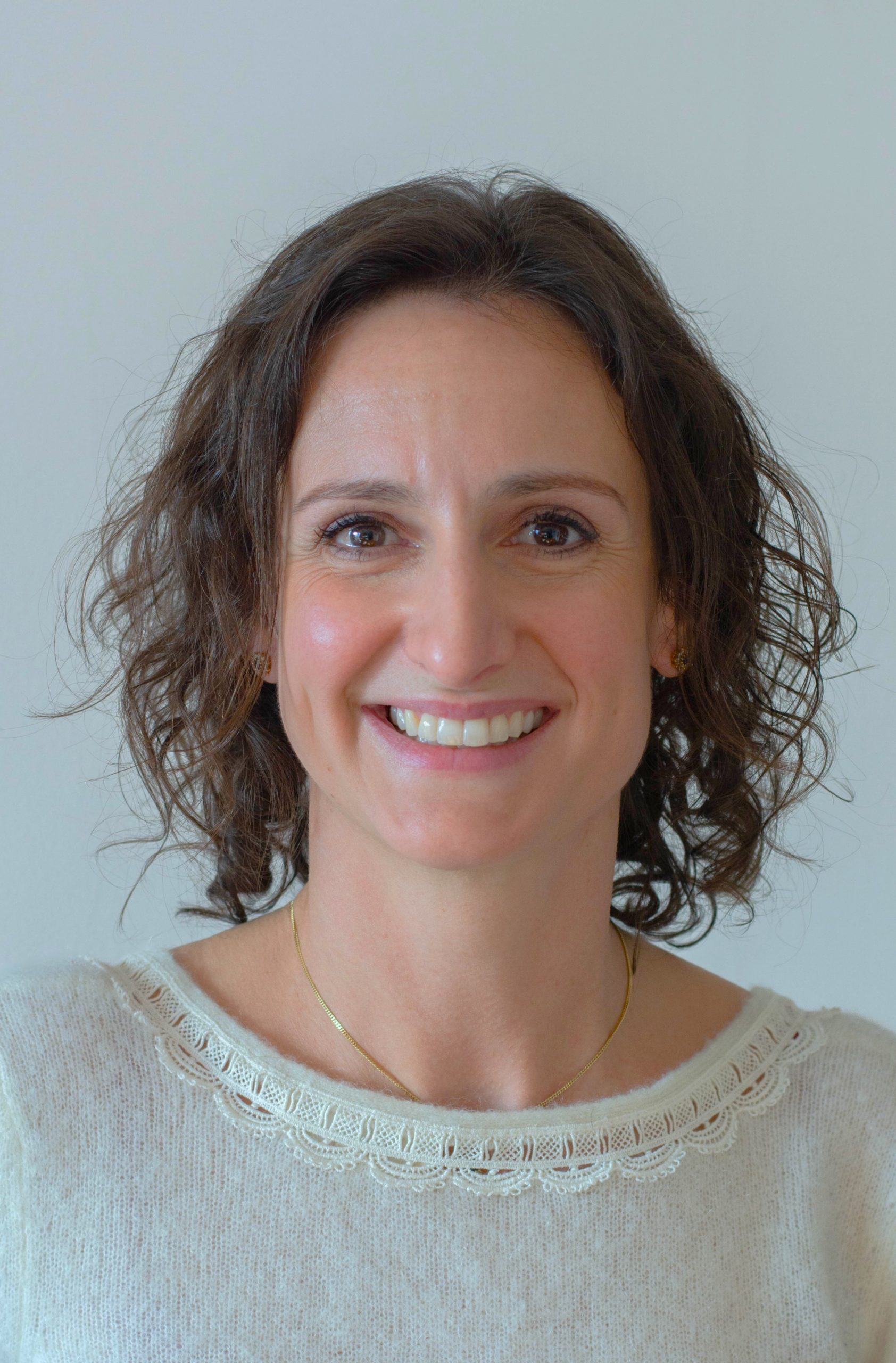 Une personne aux cheveux foncés sourit à la caméra, devant un fond gris. C'est le docteur orthodontiste Floriane le Noan