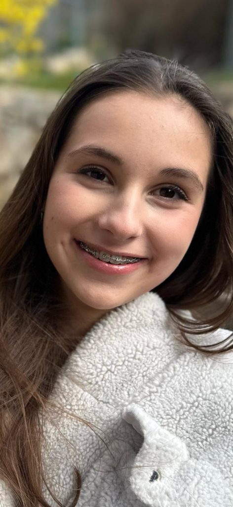 illustration urgences Une ado souriante, portant des bagues orthodontiques sur les dents. Elle a les cheveux bruns et est enveloppée dans une couverture blanche en fausse fourrure.